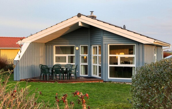 Ein eingeschossiges Haus mit Satteldach, einer Veranda mit Tisch und Stühlen sowie großen Fenstern.