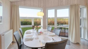 A dining area with a table set for four, large windows, and a view of the outdoors. - Friedrichskoog-Strandpark 16 (Friedrichskoog)