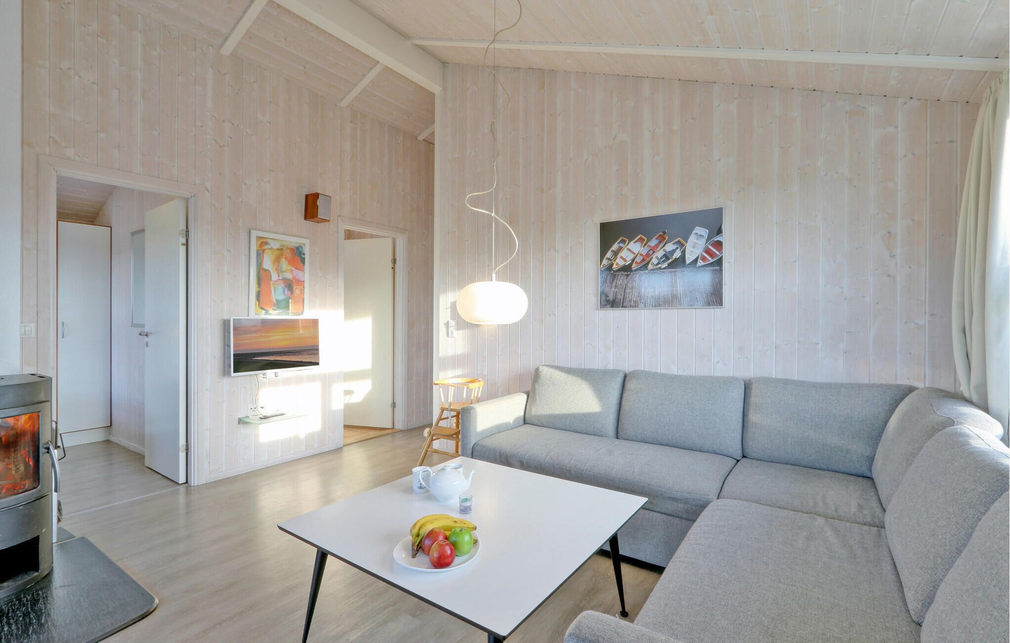 Una sala de estar moderna con un sofá gris, una mesa de centro blanca con frutas, una chimenea y un cuadro en la pared.