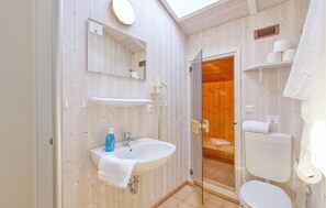 Ein kleines Badezimmer mit Holzvertäfelung, einem weißen Waschbecken, einem Spiegel, einer Toilette und einer Duschkabine.