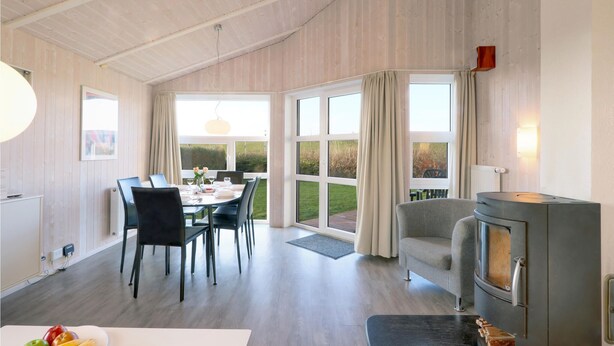 A modern dining area with a table set for four, a grey armchair, and a wood-burning stove. - Friedrichskoog-Strandpark 16 (Friedrichskoog)