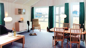 Una habitación acogedora con una mesa de madera, sillas, una lámpara, un tablero de ajedrez y vistas al exterior.