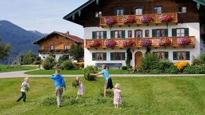 A two-story building with a balcony adorned with flowers, a well-maintained lawn, and a mountain backdrop. - Vacation apartment Sunnseitn for 4 persons, 2 bedrooms, 2 balconies, 54 sqm (Inzell)