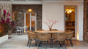 Une terrasse extérieure avec un mur en pierre, une table ronde entourée de chaises en osier et une porte vitrée donnant sur un espace intérieur.