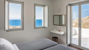Une chambre avec deux lits, une petite étagère blanche avec un miroir, et une vue sur la mer grâce à de grandes fenêtres.