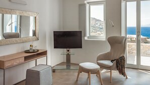 Un salon moderne doté d’un téléviseur à écran plat, d’un grand miroir, d’un fauteuil confortable et offrant une vue sur la mer grâce à de grandes portes coulissantes.