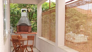 Eine Terrasse mit einem gemauerten Außenofen, Korbstühlen und einem Tisch.