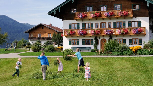 A two-story building with a balcony adorned with flowers, a well-maintained lawn, and a mountain backdrop. - Vacation apartment Himmelsstiang for 5 persons, 2 bedrooms, balcony, 57 sqm (Inzell)