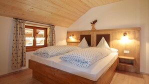 A bedroom with a wooden ceiling, a bed with patterned bedding, a window with curtains, and a wall-mounted light fixture. - Vacation apartment Himmelsstiang for 5 persons, 2 bedrooms, balcony, 57 sqm (Inzell)