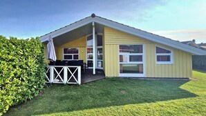 A yellow single-story house with a covered patio, a fenced deck, and a well-maintained lawn.