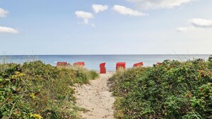 A sandy beach path leading to the sea with red beach chairs lined up on the sand.