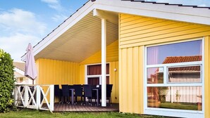 A yellow mobile home with a deck, a covered patio, and a large window.