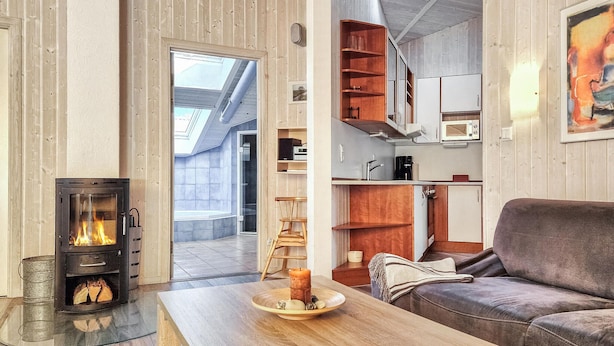 A cozy living room with a fireplace, a wooden table with a candle, a sofa, and a kitchen area with cabinets and a microwave.