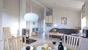Un salon chaleureux avec une cheminée, un canapé, une table à manger où sont servis des plats et du vin, et un téléviseur.