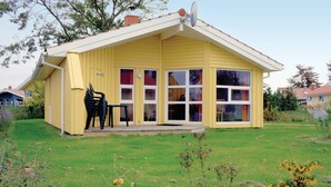 Une maison jaune d’un seul étage, dotée d’un patio couvert, d’une antenne parabolique et d’un petit jardin.