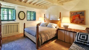 A bedroom with a wooden bed, two windows with shutters, a radiator, a bedside table with a lamp, and a painting on the wall. - Stunning private villa with WIFI, private pool, TV, patio and panoramic view, close to Lucca (Santo Stefano)