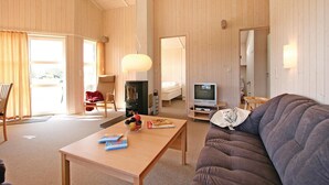 Una habitación acogedora con detalles de madera, un sofá, un televisor, una mesa con revistas y una silla.