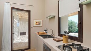 A compact kitchen with a gas stove, sink, and a window with a view of greenery. - Casa Carol - Blu - Independent Villa Modica Area (Scicli)
