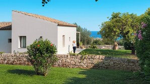 A white building with a stone wall in front, a clear blue sky, and a view of the sea. - Casa Carol - Blu - Independent Villa Modica Area (Scicli)