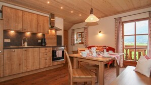 Ein Holzblockhaus-Interieur mit Küche, Essbereich und einem großen Fenster mit Blick ins Freie.