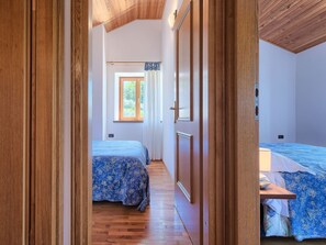 A bedroom with two beds, wooden flooring, a window with curtains, and a wooden ceiling.