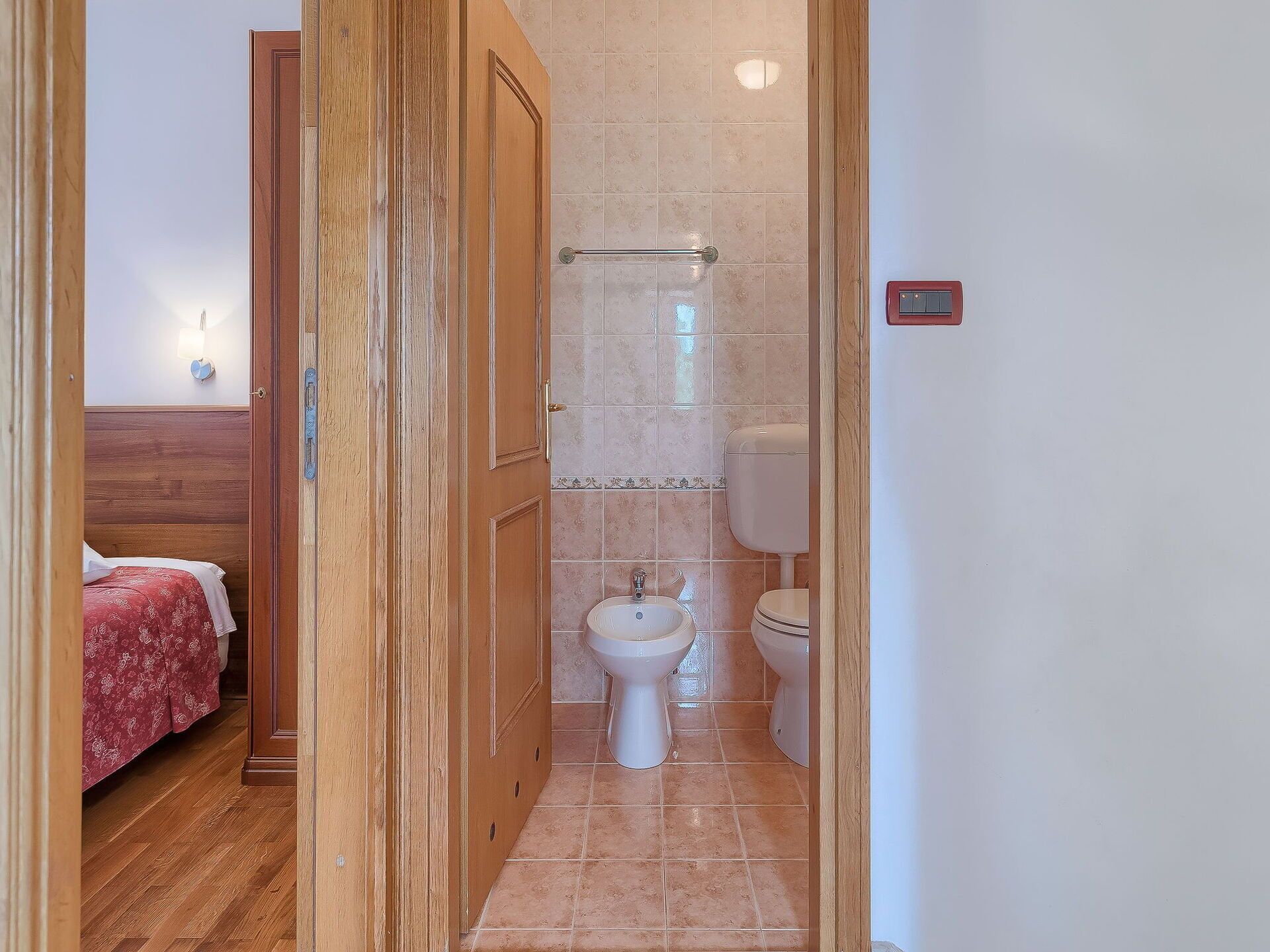 A narrow hallway leading to a bathroom with a bidet, toilet, and a wooden door.