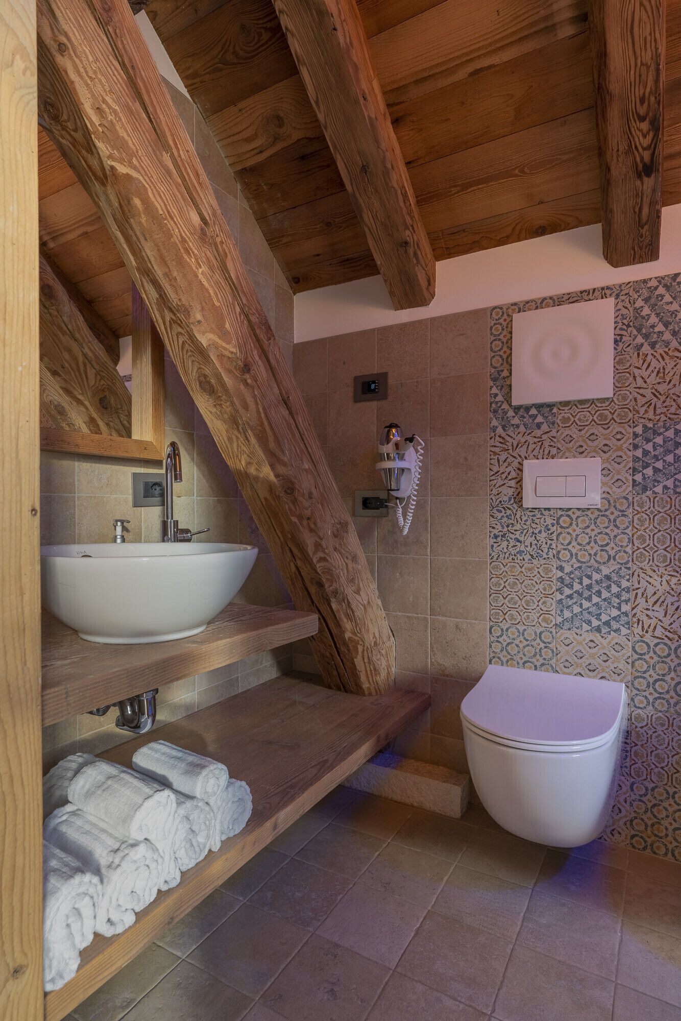 Une salle de bain avec un plafond en bois, un lavabo blanc, des toilettes et des carreaux à motifs.