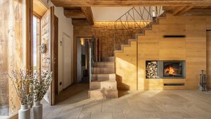 A modern interior with a wooden staircase, a fireplace, and a view through a large window. - Casera Cornolera (Chies d´Alpago)