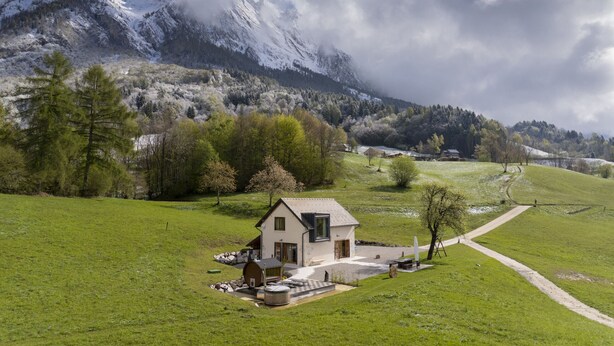 A modern house with a large window, a stone wall, and a wooden barrel in the yard. - Casera Cornolera (Chies d´Alpago)