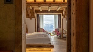 A bedroom with a wooden ceiling and a bed. There is a window with curtains and a view of the outside. - Casera Cornolera (Chies d´Alpago)