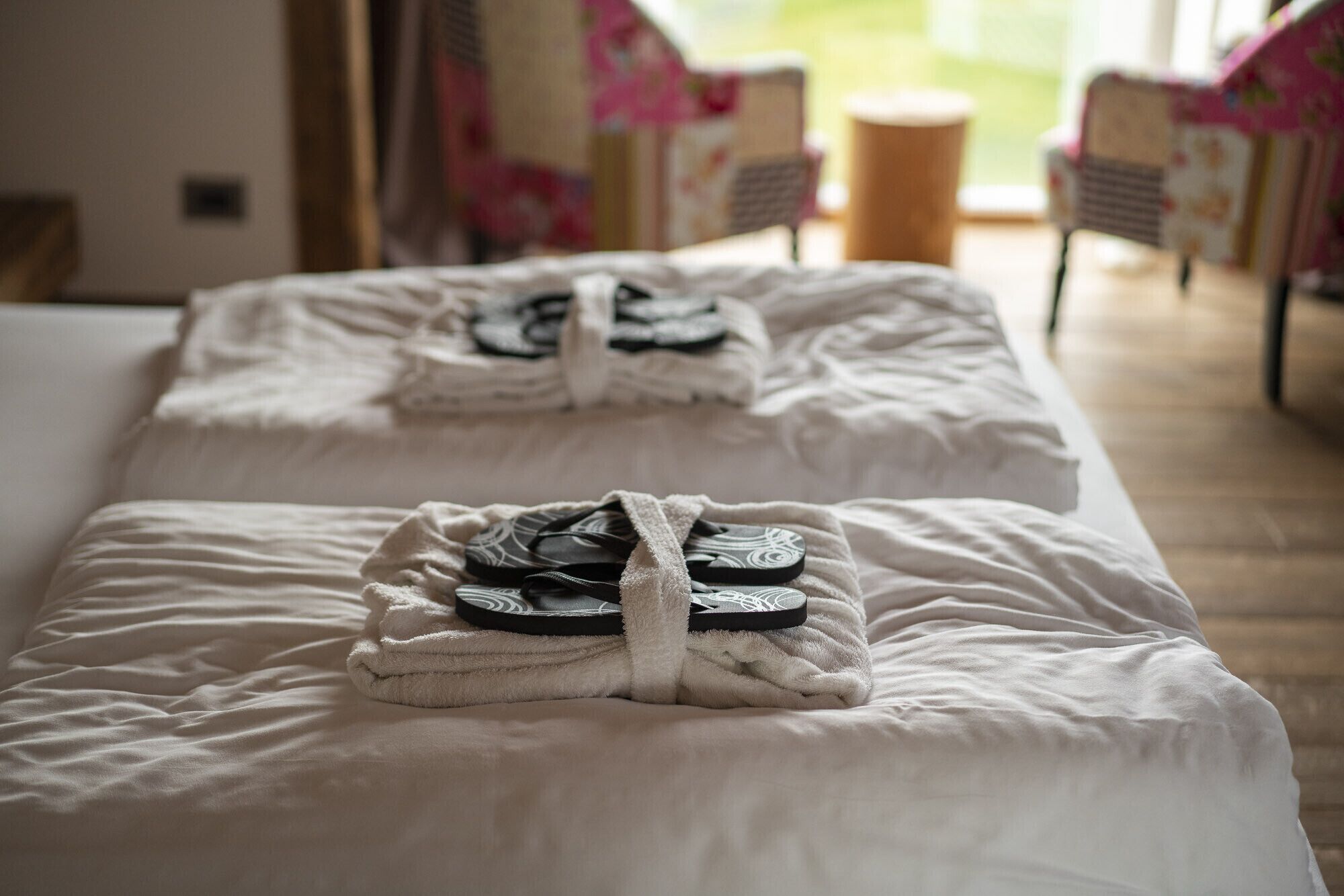A hotel room with two beds, each with a towel and flip-flops placed on them.