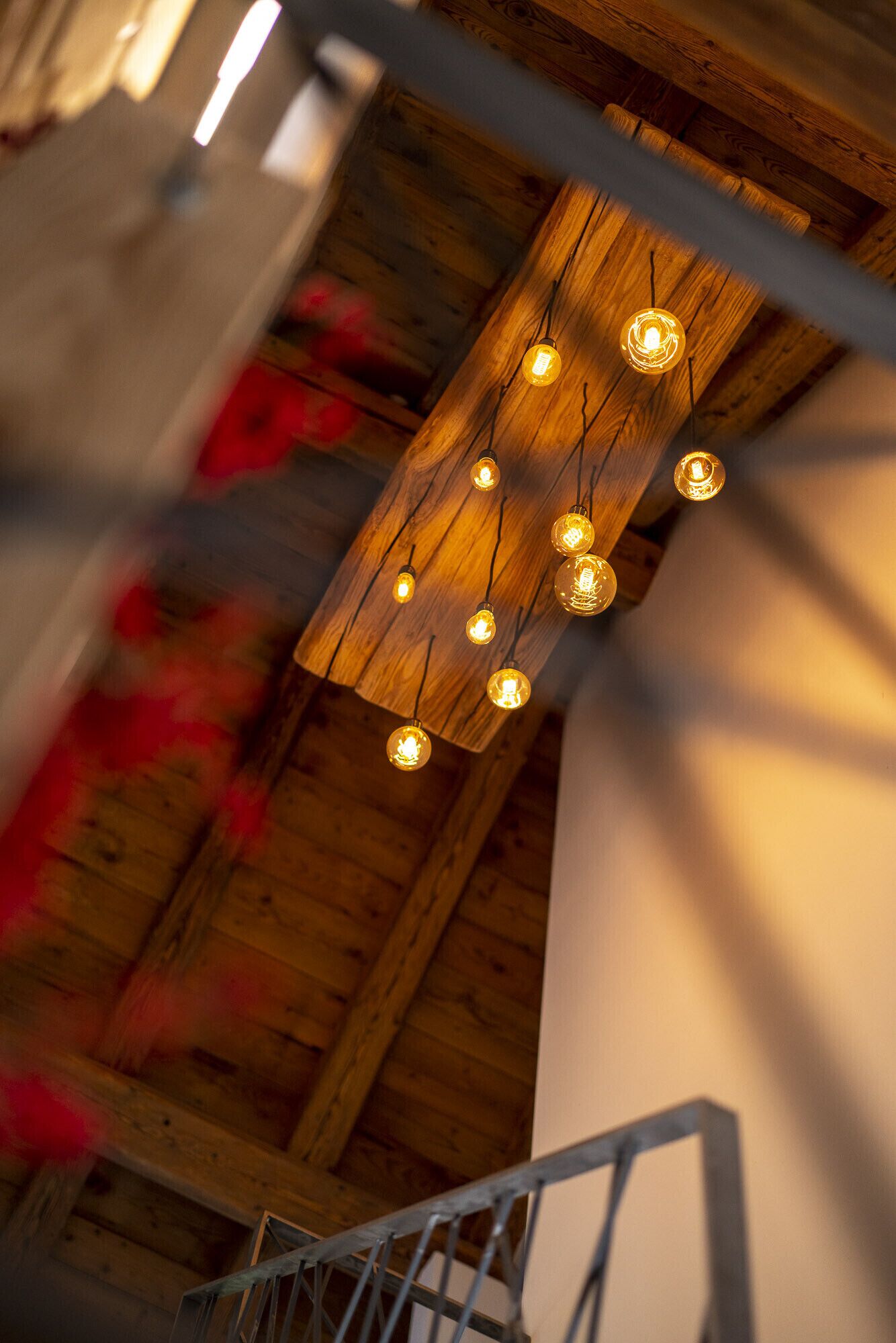 A staircase with a wooden railing and a ceiling with exposed beams and hanging light fixtures.