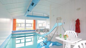 Ein Hallenbad mit Rutsche, ein kleiner Tisch mit Getränken und ein rotes Handtuch an der Wand.