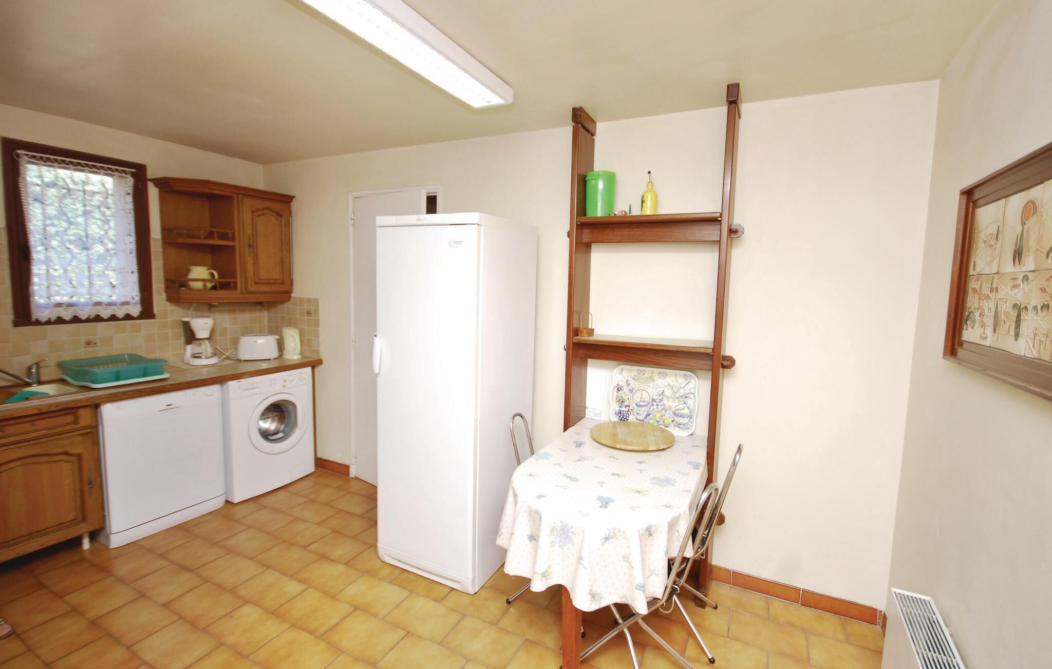 A compact kitchen with a washing machine, a refrigerator, and a dining table with a floral tablecloth.