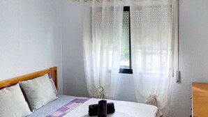 Ein Schlafzimmer mit einem Bett, einem Fenster mit transparenten Vorhängen und einem Holzkopfteil.