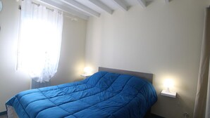 A bedroom with a large bed, two bedside lamps, and a window with sheer curtains.