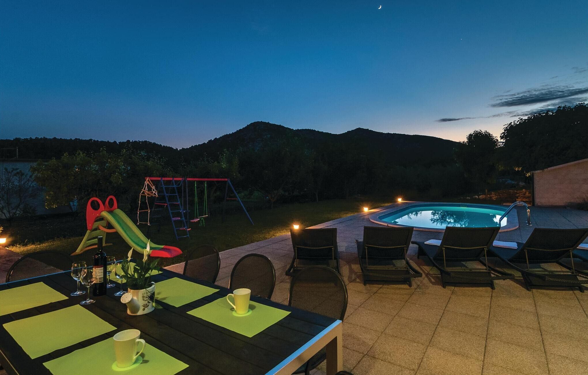 An outdoor patio with a pool, dining area, and children's play equipment.