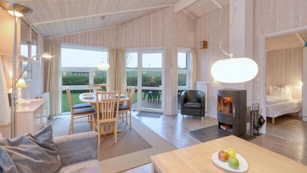 A spacious living area with a dining table, chairs, a sofa, a fireplace, and large windows. - Friedrichskoog-Strandpark 18 (Friedrichskoog)