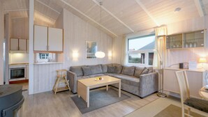 A cozy living room with a sofa, a coffee table, and a small kitchen area with cabinets and a stove. - Friedrichskoog-Strandpark 18 (Friedrichskoog)