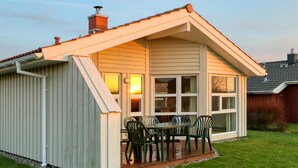 A small, single-story house with a sloped roof, a porch with a table and chairs, and a chimney. - Friedrichskoog-Strandpark 18 (Friedrichskoog)
