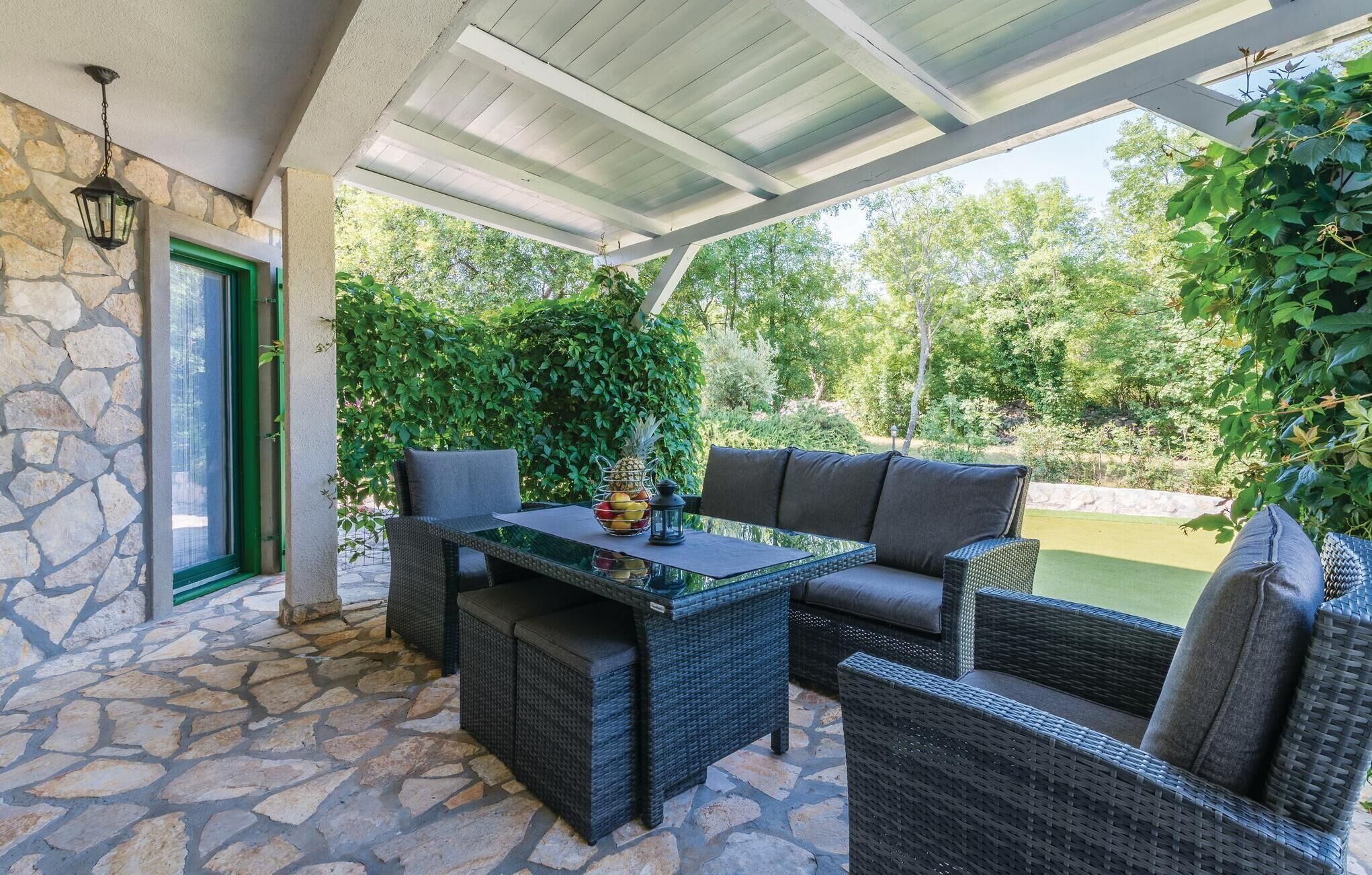 Un patio cubierto con mobiliario de mimbre, una mesa de cristal y una pared de piedra.