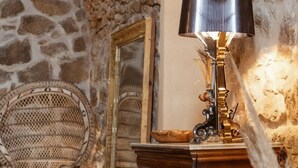 Une pièce avec un mur en pierre, une table en bois avec une lampe, un miroir et des meubles en osier.