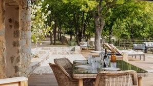 Un espace extérieur aménagé pour les repas, avec des meubles en osier, des murs en pierre et une vue sur les arbres et un sentier.