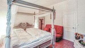 Una cama con dosel, una silla roja, un armario y una mesita con fruta.