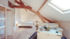 Un dormitorio acogedor en el ático, con techo inclinado, una cama, un sofá y una pequeña mesa con un jarrón de flores.