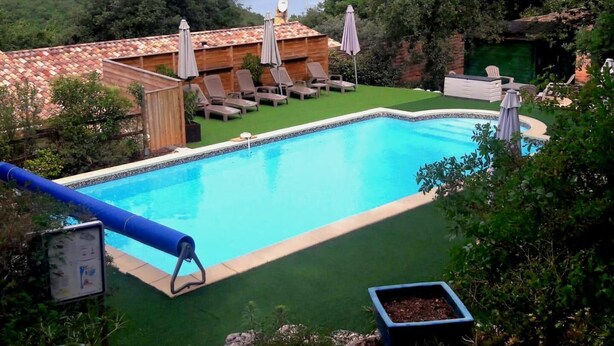 Una piscina con sillones y sombrillas, rodeada de vegetación y vistas a un lago.