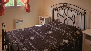 Un dormitorio con cama, mesita de noche, radiador y ventana con cortinas.