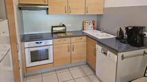 Una cocina compacta con armarios de madera, horno integrado, lavavajillas, tostadora y cafetera.