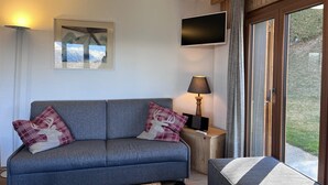 A modern living room with a grey sofa, two red and white patterned pillows, a side table with a lamp, a flat-screen TV, and a large window with curtains. - Greppons N 002 - MOUNTAIN apartment 9 pers (Veysonnaz)