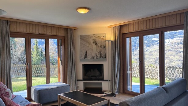 A cozy living room with a fireplace, large windows, and a view of the outdoors. - Greppons N 002 - MOUNTAIN apartment 9 pers (Veysonnaz)